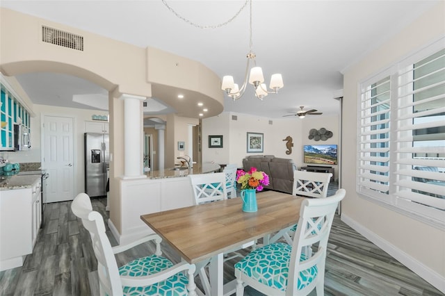 dining space featuring ceiling fan with notable chandelier, sink, hardwood / wood-style floors, and ornate columns