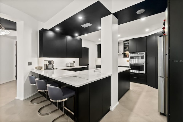 kitchen with light tile patterned floors, a breakfast bar area, light stone countertops, kitchen peninsula, and stainless steel double oven