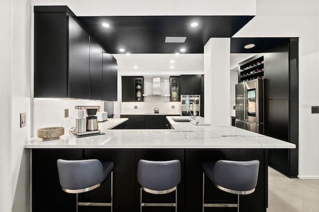 kitchen with sink, a breakfast bar area, kitchen peninsula, stainless steel appliances, and wall chimney range hood