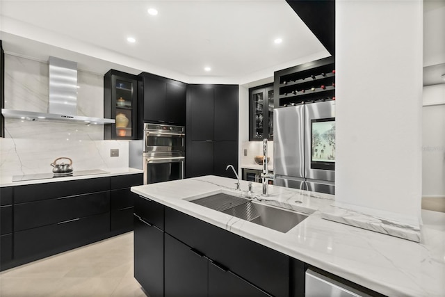 kitchen with wall chimney range hood, light stone countertops, sink, and appliances with stainless steel finishes