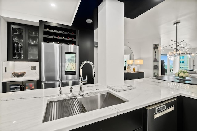 kitchen with stainless steel refrigerator, dishwasher, sink, hanging light fixtures, and light stone countertops