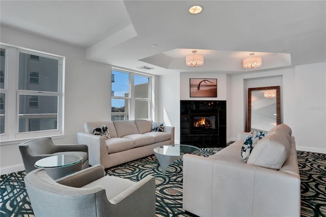 living room featuring a tray ceiling and a tiled fireplace