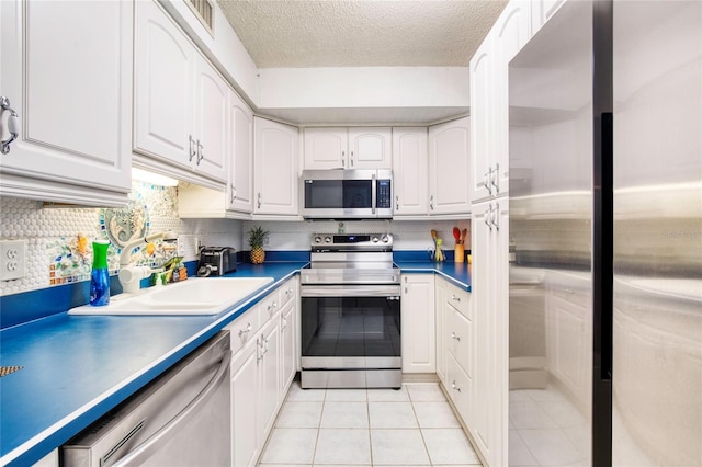 kitchen featuring stainless steel appliances, sink, light tile patterned floors, and white cabinets