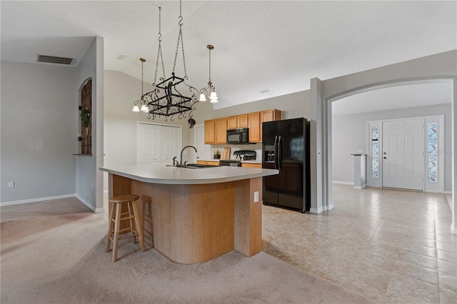 kitchen with lofted ceiling, decorative light fixtures, an island with sink, light colored carpet, and black appliances