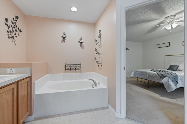 bathroom featuring ceiling fan, vanity, a textured ceiling, and tiled tub