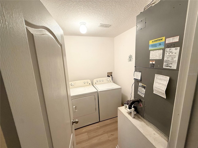 washroom featuring heating unit, washer and clothes dryer, light hardwood / wood-style flooring, and a textured ceiling