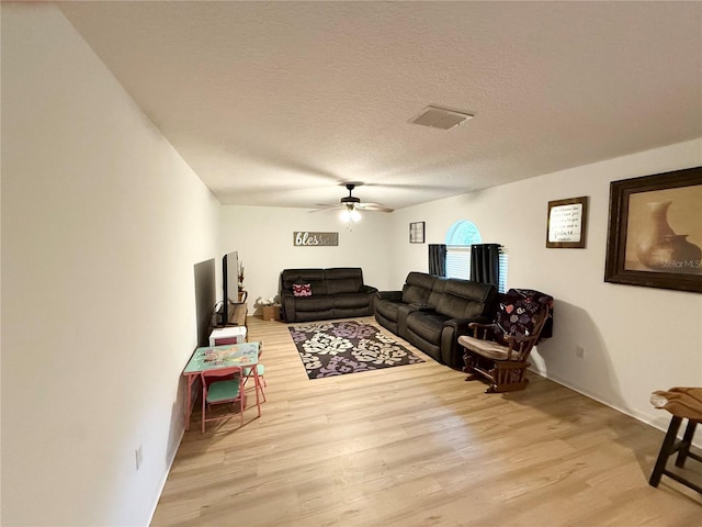 living room with ceiling fan, a textured ceiling, and light wood-type flooring