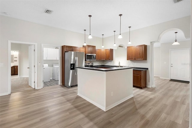 kitchen featuring stainless steel appliances, a center island, a high ceiling, washer and dryer, and decorative light fixtures