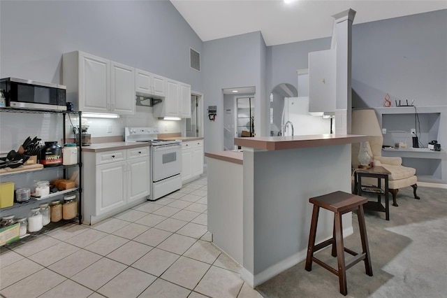 kitchen with light tile patterned flooring, a kitchen breakfast bar, kitchen peninsula, white appliances, and white cabinets