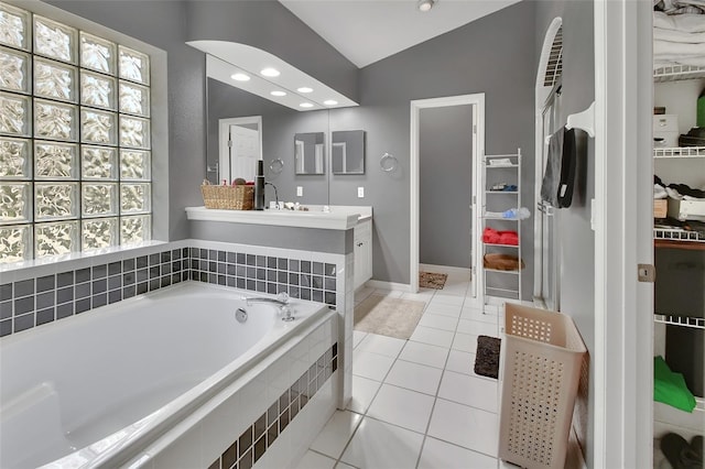 bathroom with a relaxing tiled tub, lofted ceiling, tile patterned flooring, and vanity