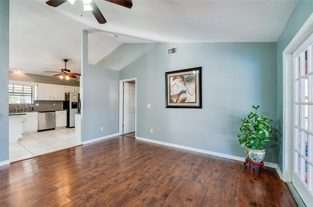 unfurnished living room with vaulted ceiling, sink, ceiling fan, and light wood-type flooring