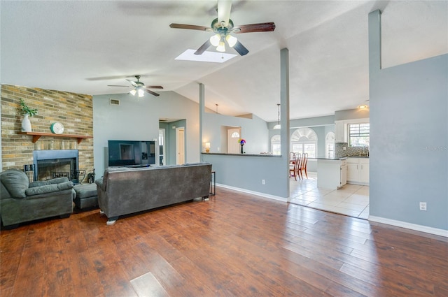 living room featuring lofted ceiling, a fireplace, ceiling fan, and light wood-type flooring