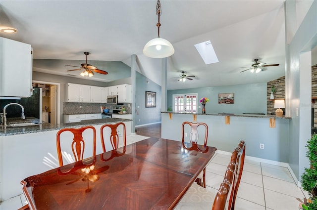 tiled dining room featuring ceiling fan, lofted ceiling with skylight, and sink