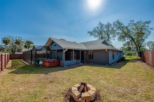 back of property featuring a hot tub, a lawn, glass enclosure, and an outdoor fire pit