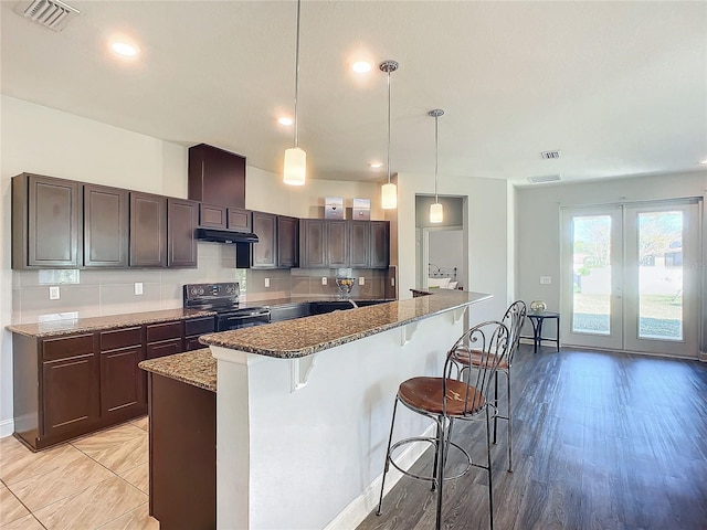 kitchen featuring decorative light fixtures, a breakfast bar, decorative backsplash, and black range with electric cooktop