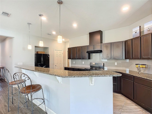 kitchen featuring stone counters, electric range oven, a kitchen bar, decorative backsplash, and black fridge