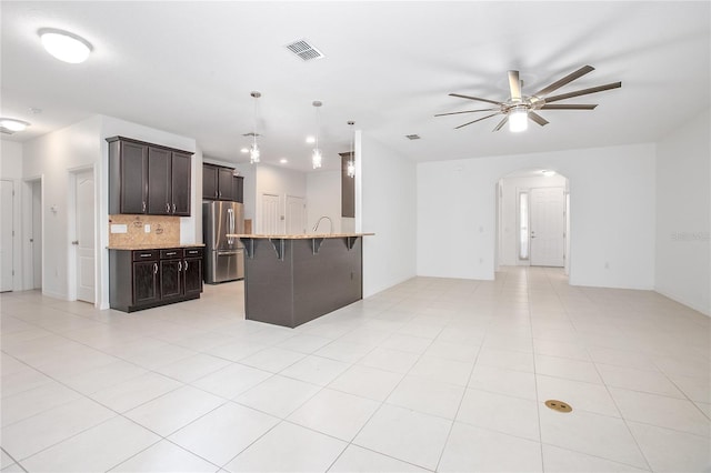 kitchen featuring stainless steel fridge, a breakfast bar, ceiling fan, hanging light fixtures, and decorative backsplash