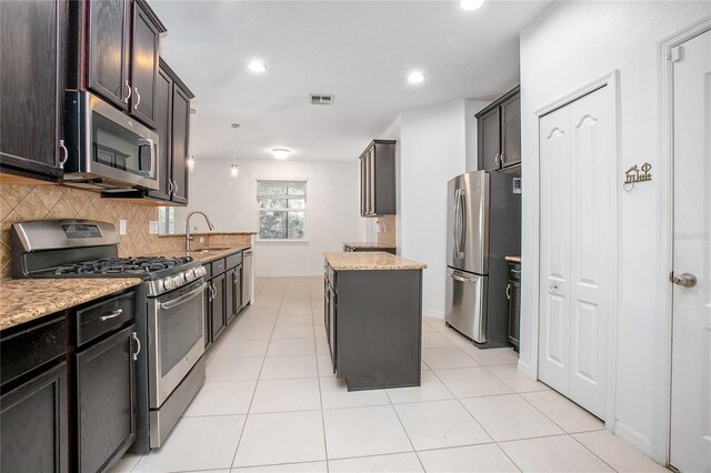 kitchen with pendant lighting, appliances with stainless steel finishes, light stone counters, tasteful backsplash, and a kitchen island