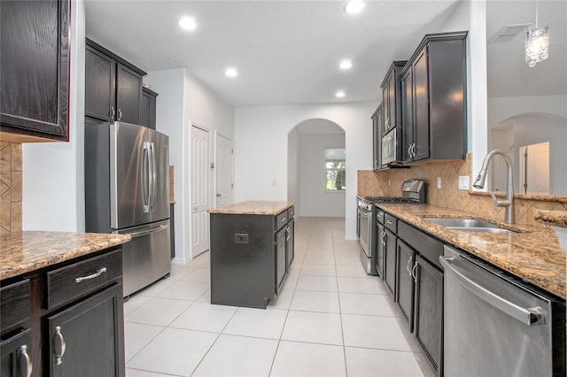 kitchen with light tile patterned flooring, sink, appliances with stainless steel finishes, a kitchen island, and light stone countertops