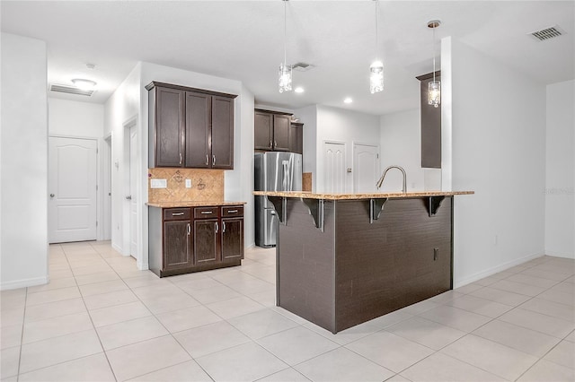 kitchen with a breakfast bar, decorative light fixtures, light tile patterned floors, stainless steel refrigerator, and backsplash