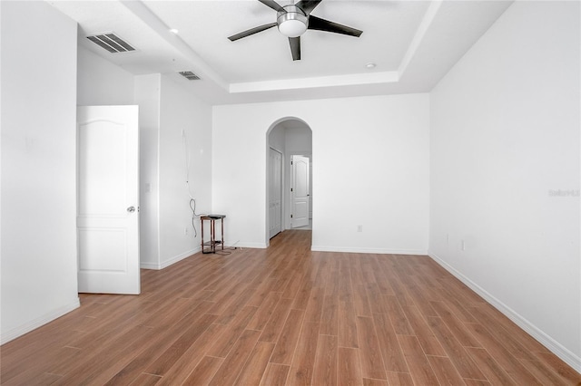 empty room with ceiling fan, a raised ceiling, and light wood-type flooring