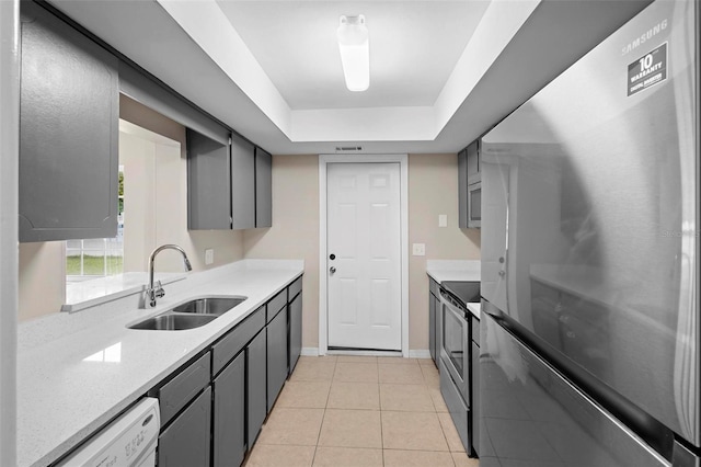 kitchen featuring appliances with stainless steel finishes, sink, gray cabinetry, light tile patterned floors, and a tray ceiling