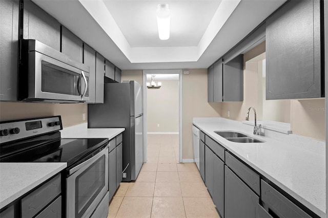 kitchen featuring light tile patterned flooring, sink, gray cabinetry, a tray ceiling, and stainless steel appliances