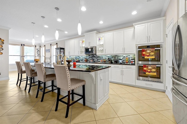 kitchen with an island with sink, white cabinetry, hanging light fixtures, ornamental molding, and stainless steel appliances