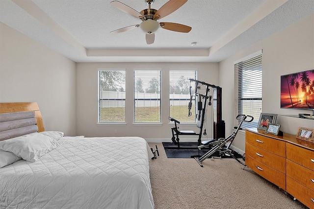 carpeted bedroom with a tray ceiling, a textured ceiling, and ceiling fan