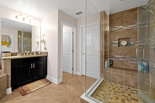 bathroom with a shower with door, vanity, tile patterned floors, and a textured ceiling