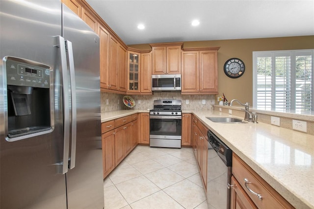 kitchen with sink, light tile patterned floors, appliances with stainless steel finishes, light stone countertops, and decorative backsplash