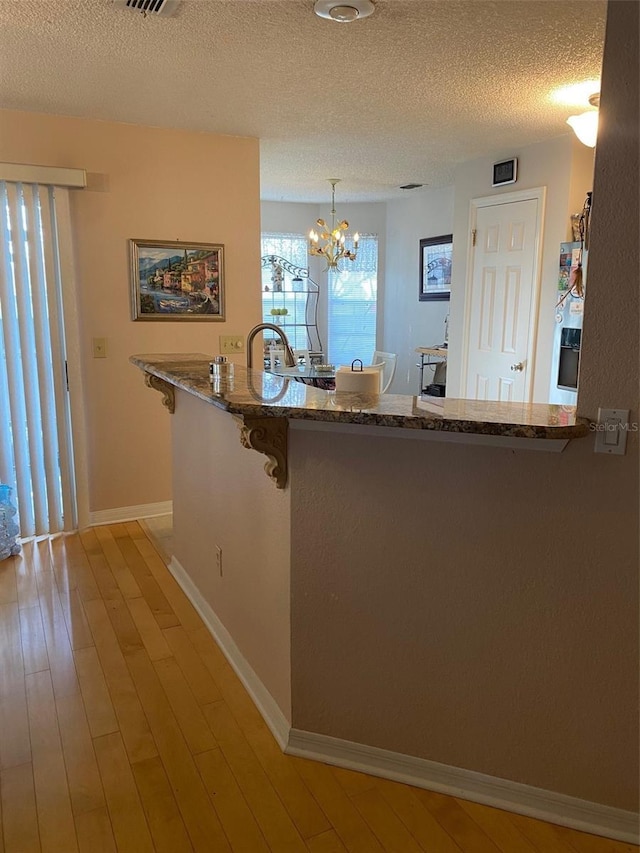 kitchen featuring decorative light fixtures, kitchen peninsula, a textured ceiling, and light wood-type flooring