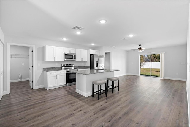 kitchen featuring a breakfast bar, stainless steel appliances, white cabinets, a center island with sink, and dark stone counters