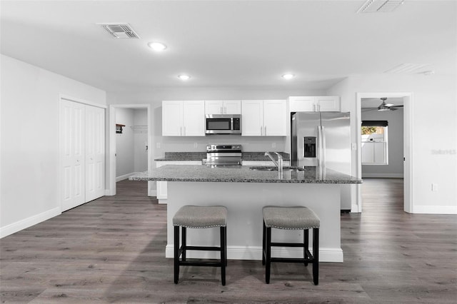 kitchen with an island with sink, appliances with stainless steel finishes, dark stone countertops, and white cabinets