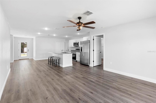 kitchen with a breakfast bar, ceiling fan, appliances with stainless steel finishes, a kitchen island with sink, and white cabinets