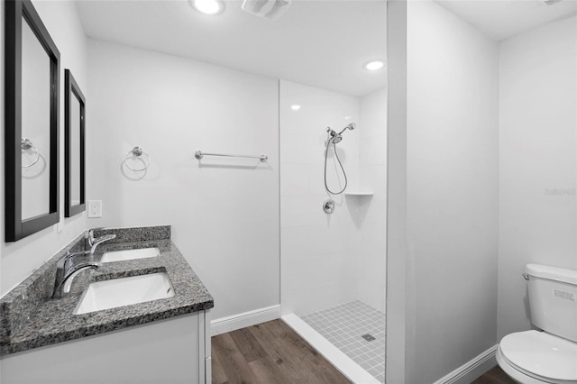 bathroom with wood-type flooring, toilet, vanity, and a tile shower