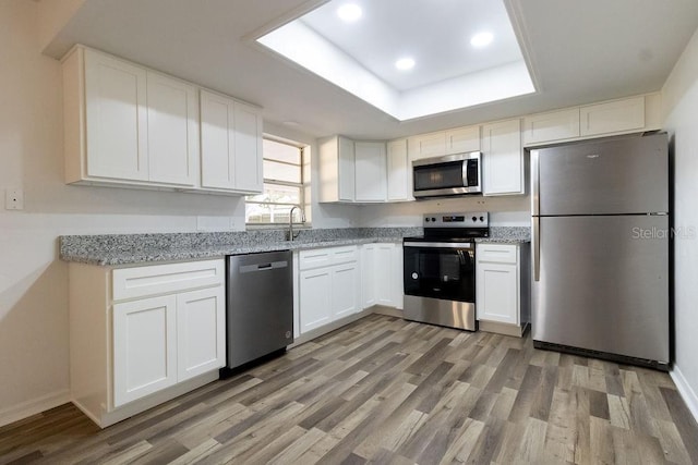 kitchen featuring white cabinetry, sink, a tray ceiling, stainless steel appliances, and light hardwood / wood-style flooring