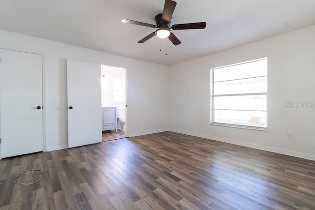 unfurnished bedroom featuring ceiling fan, ensuite bathroom, dark hardwood / wood-style flooring, and multiple windows