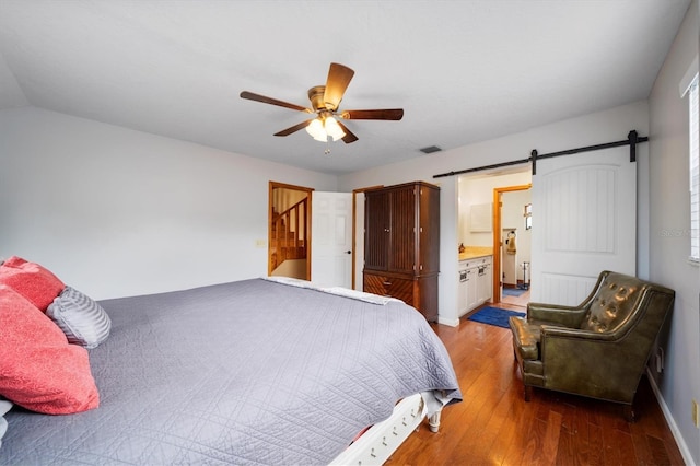 bedroom with hardwood / wood-style flooring, a barn door, connected bathroom, and ceiling fan