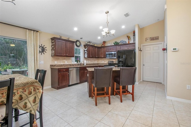 kitchen with appliances with stainless steel finishes, pendant lighting, a center island, light stone counters, and dark brown cabinetry