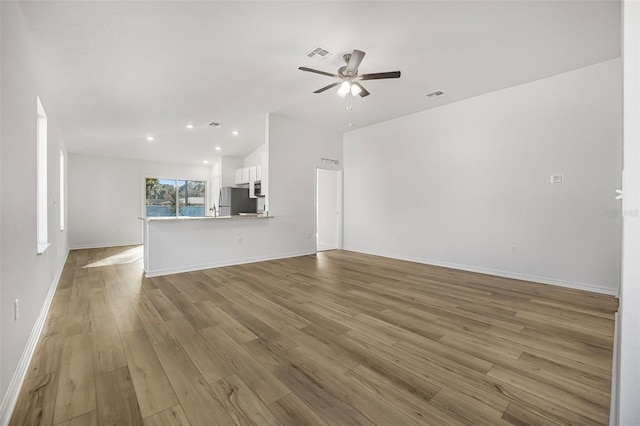 unfurnished living room with vaulted ceiling, ceiling fan, and light wood-type flooring