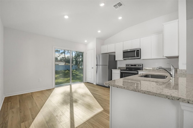 kitchen with appliances with stainless steel finishes, sink, white cabinets, light stone countertops, and light wood-type flooring