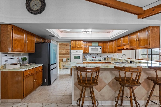 kitchen with a skylight, sink, a kitchen breakfast bar, a tray ceiling, and white appliances