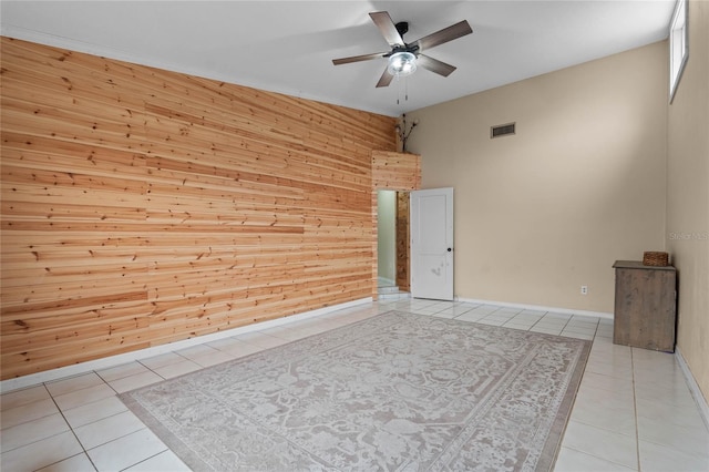 tiled empty room featuring wooden walls and ceiling fan