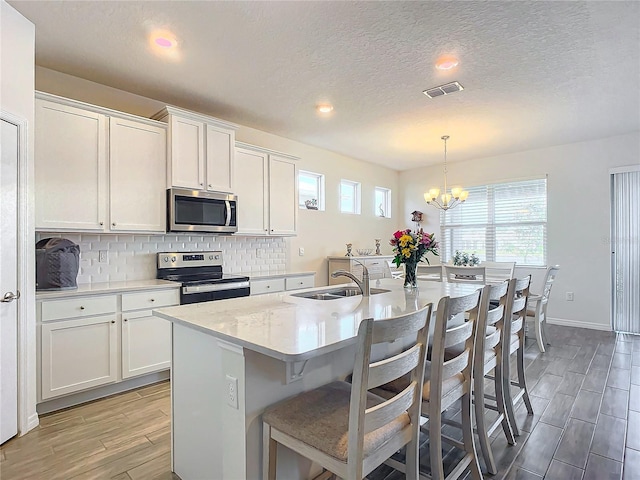 kitchen featuring white cabinetry, decorative light fixtures, an island with sink, and appliances with stainless steel finishes