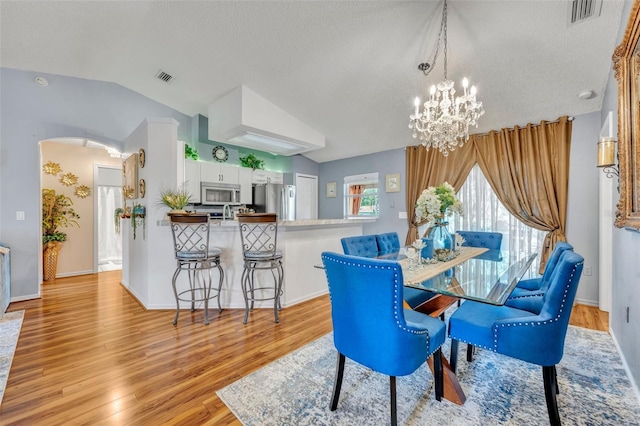 dining space with vaulted ceiling, a chandelier, a textured ceiling, and light wood-type flooring