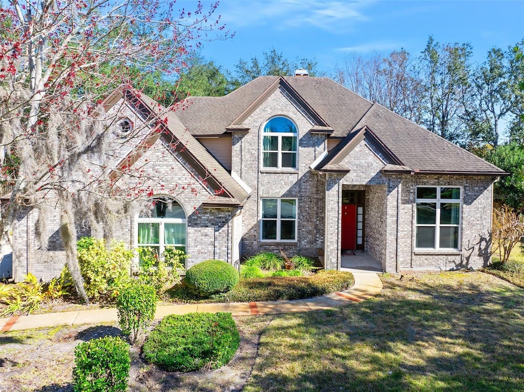 view of front of house featuring a chimney, brick siding, roof with shingles, and a front yard