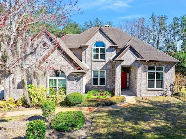 view of front of house featuring a chimney, brick siding, roof with shingles, and a front yard