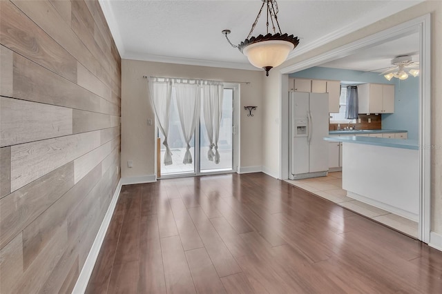 interior space with crown molding, wood walls, ceiling fan, and light wood-type flooring