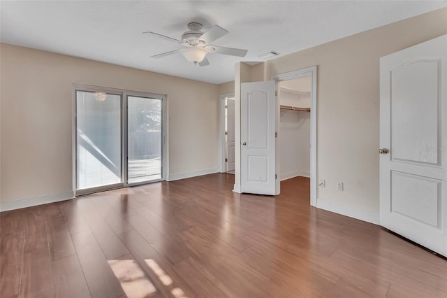 unfurnished bedroom featuring ceiling fan, a spacious closet, access to exterior, and dark hardwood / wood-style flooring